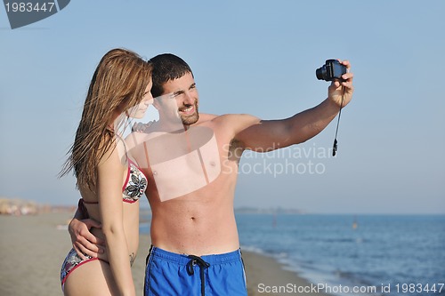 Image of happy young couple in love taking photos on beach