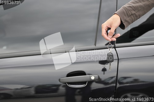 Image of male hand holding car key with new black car in background