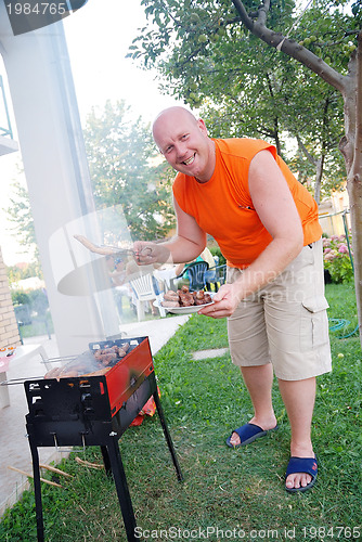 Image of happy man preparing sausages on grill