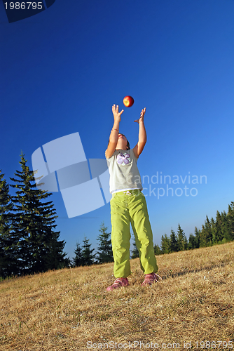 Image of happy girl throwing apple outside