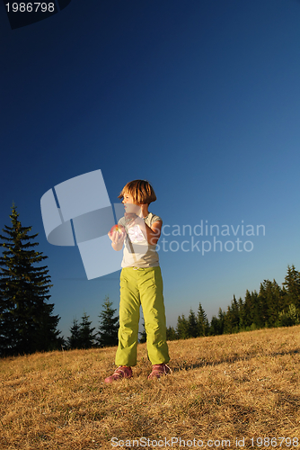 Image of happy girl throwing apple outside