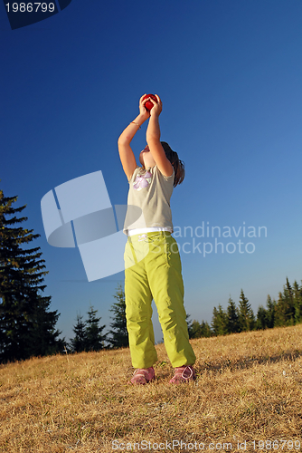 Image of happy girl throwing apple outside