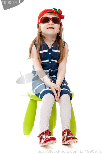 Image of little girl in a red hat and sunglasses sitting on a green chair