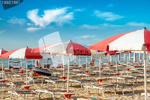Image of red and white umbrellas and sunlongers on the sandy beach