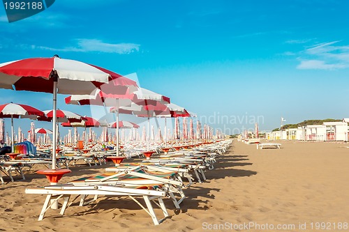 Image of red and white umbrellas and sunlongers on the sandy beach