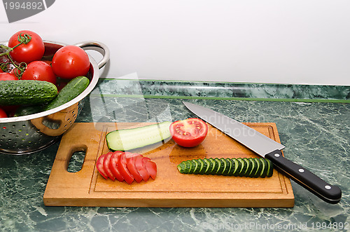 Image of red tomato and green cucumbers slices with knife on board