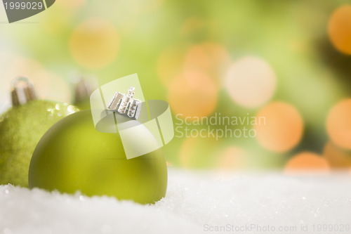 Image of Green Christmas Ornaments on Snow Over an Abstract Background