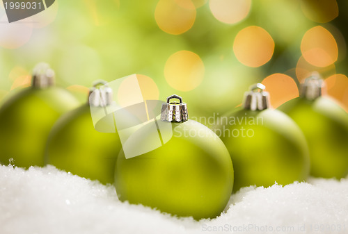 Image of Green Christmas Ornaments on Snow Over an Abstract Background