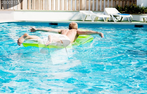 Image of young man is swimming with air mattress in pool