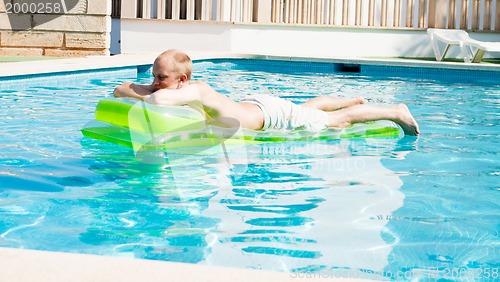 Image of young man is swimming with air mattress in pool