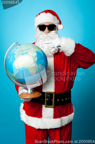 Image of Stylish Santa in dark shades pointing at the globe