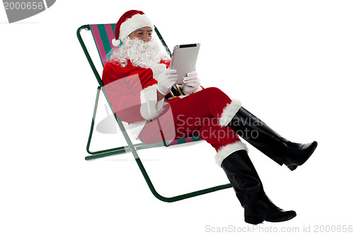 Image of Kris Kringle relaxing and using electronic tablet