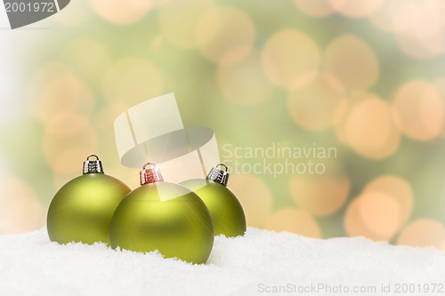 Image of Green Christmas Ornaments on Snow Over an Abstract Background