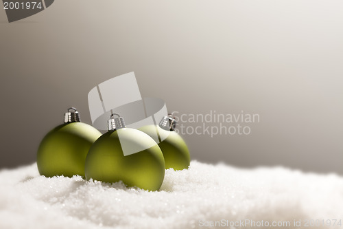 Image of Green Christmas Ornaments on Snow Over a Grey Background