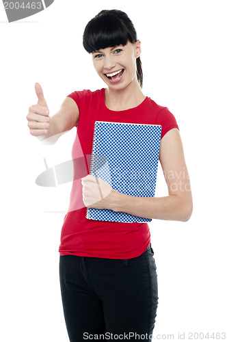 Image of Pretty teenager holding notebook and gesturing thumbs up