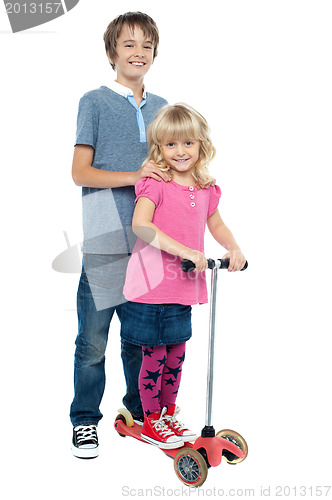 Image of Brother holding her sister as she rides her toy scooter
