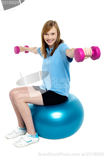 Image of Girl sitting on pilates ball and doing dumbbells