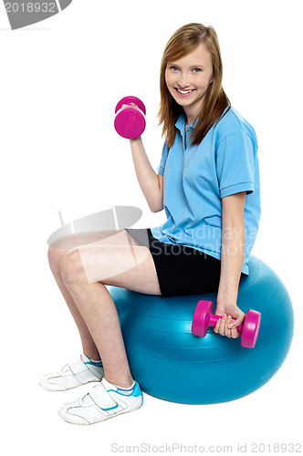 Image of Pretty teen seated on a blue pilate ball doing dumbbells