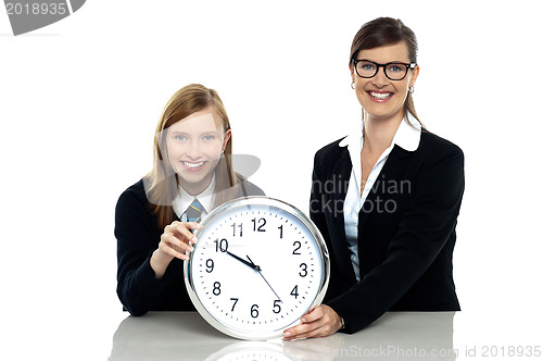 Image of Pretty student holding clock with her teacher