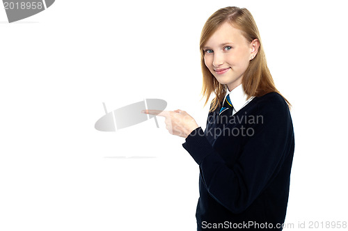 Image of Pretty schoolgirl pointing towards copy space area