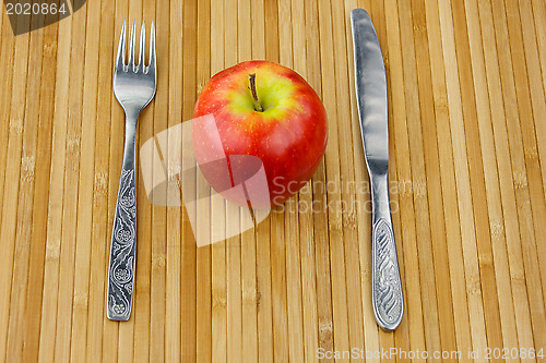 Image of apple lying on a bamboo napkin with cutlery