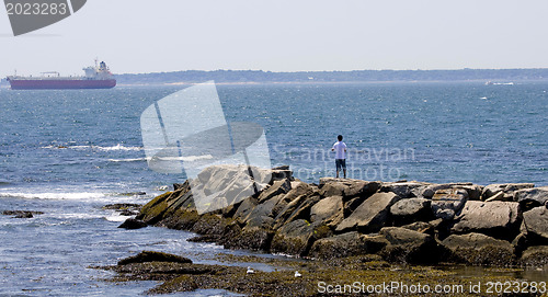 Image of Rocky breakwater with young man and with a boat in the backgroun