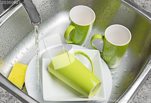 Image of Washing green cups and plates in the kitchen sink