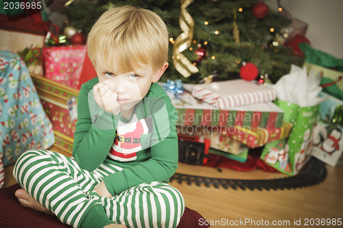 Image of Young Grumpy Boy Sitting Near Christmas Tree