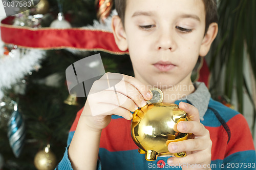 Image of Little boy puts a coin in cash pig