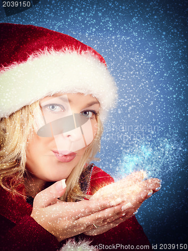 Image of Joyful pretty woman blowing stars in red santa claus hat 