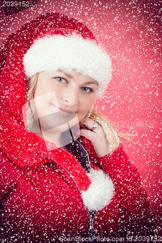 Image of Joyful pretty woman in red santa claus hat smiling with snowflakes