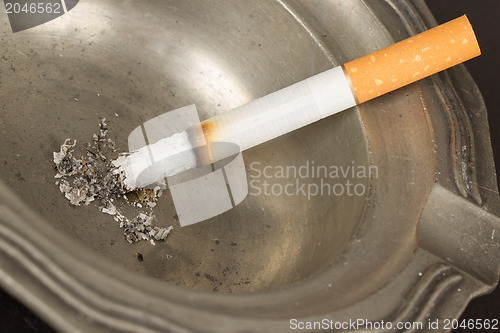 Image of Burning cigarette in an old tin ashtray