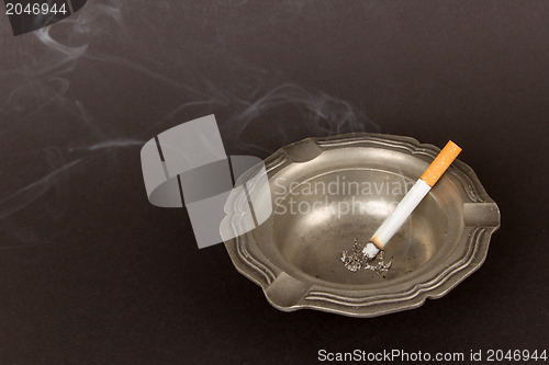 Image of Burning cigarette in an old tin ashtray