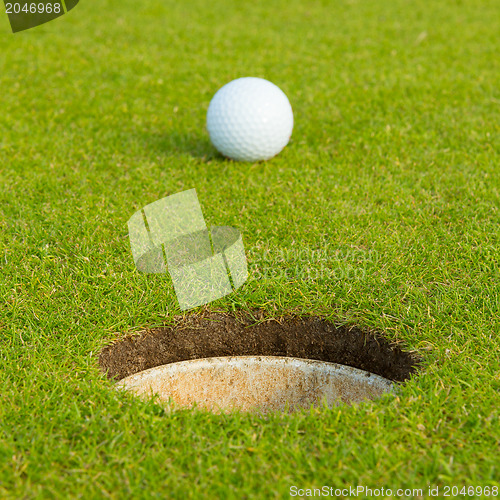 Image of Golf ball in front of the hole, focus on the hole