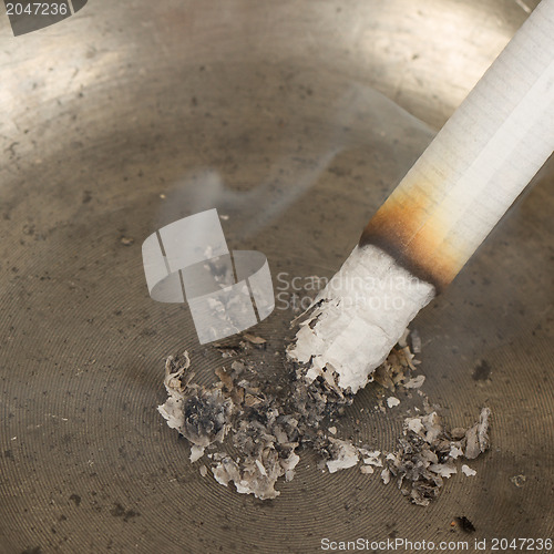 Image of Burning cigarette in an old tin ashtray