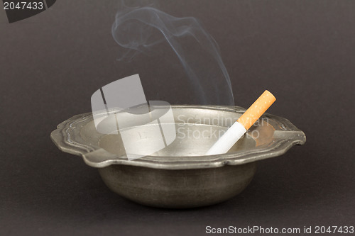 Image of Burning cigarette in an old tin ashtray