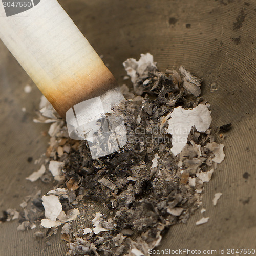 Image of Burning cigarette in an old tin ashtray