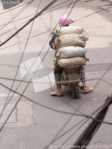 Image of Typical Hanoi; Man with heavy load on scooter drives through Han