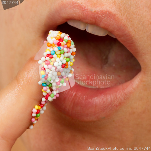 Image of Woman lips and finger with multicolored pearls 