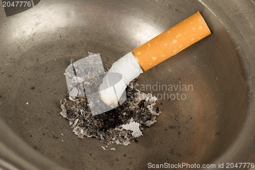 Image of Burning cigarette in an old tin ashtray