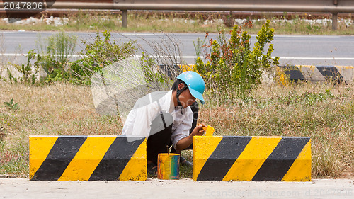 Image of Man painting roadworks barriers on a road in Vietnam