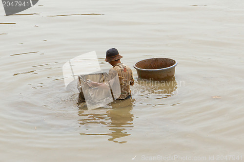 Image of A vietnamese fisherman is searching for shells in the water