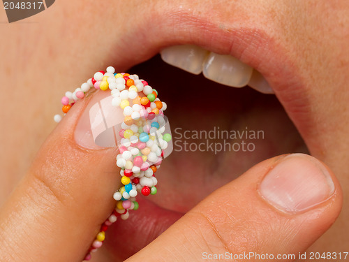 Image of Woman lips and finger with multicolored pearls 