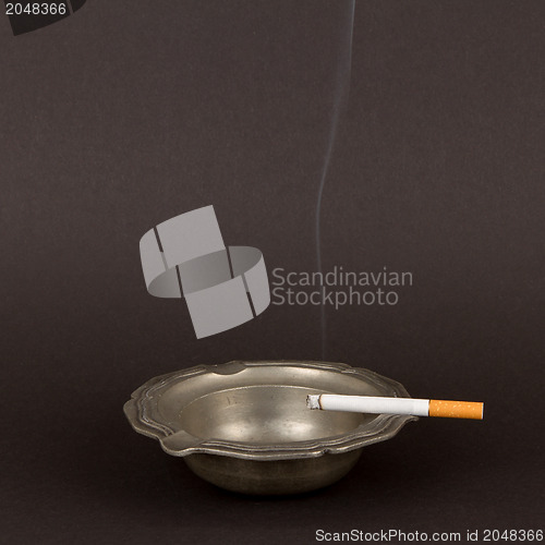 Image of Burning cigarette in an old tin ashtray