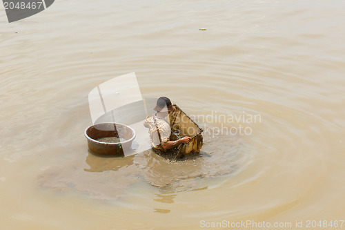 Image of A vietnamese fisherman is searching for shells in the water