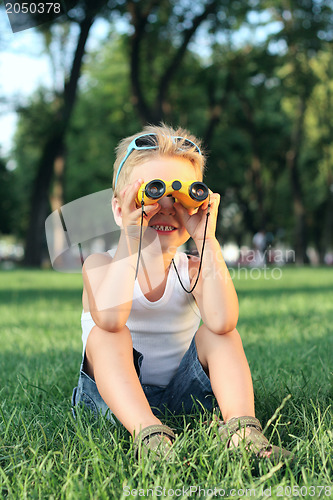 Image of Little boy sitting in the park with a binoculars