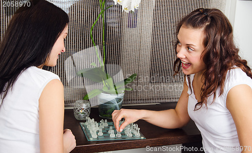 Image of Two young beautiful girlfriends play chess at home