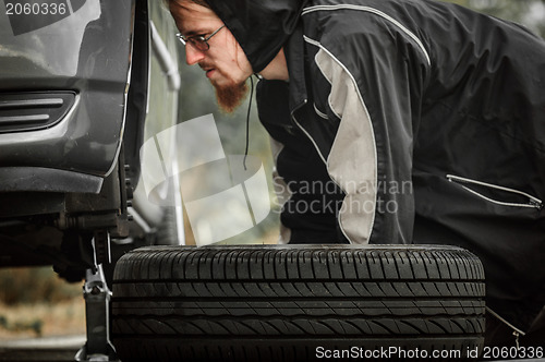 Image of Young adult inspecting the wheel of a car