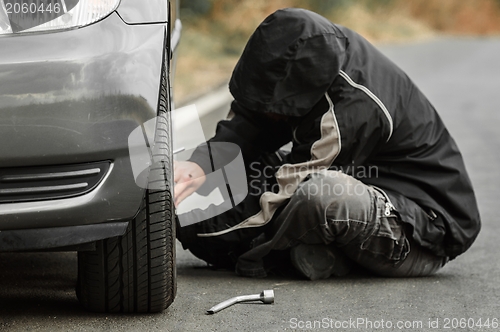 Image of Young man repairing car outdoors