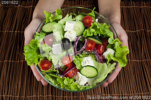 Image of Hands holding salad in a glass bowl 